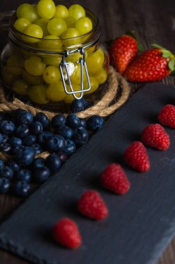 Bodegon meyvesi, levhada taze çilek, yaban mersini ve yıllanmış üzümlerle dolu cam kavanoz.