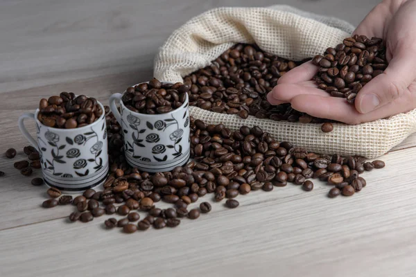 Coffee beans in a rustic coffee bag, full cups and hand holding the coffee