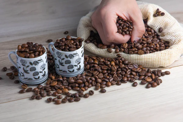 Coffee beans in a rustic coffee bag, full cups and hand holding the coffee