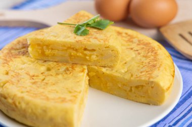 Yumurta ve tahta kaşıkla beyaz tabakta kesilmiş İspanyol patates omleti.