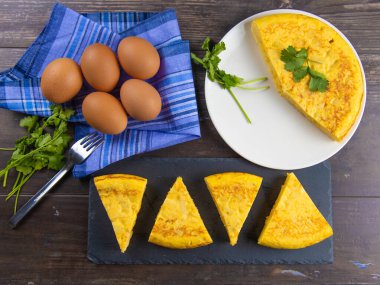 Beyaz tabakta İspanyol patates omleti porsiyonları ve yumurta ve maydanozlu ahşap tahta, orijinal fotoğraf.