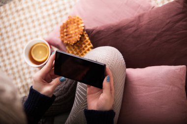 Yatakta sıcak fincan çay ile akıllı telefon tutarak el görünümünü yukarıda.