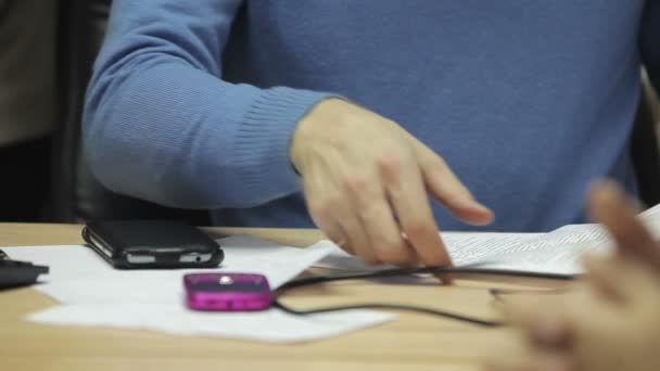 Бизнесмен читает контракт, перелистывая последнюю страницу. На столе два мобильных телефона. Руки крупным планом — стоковое видео