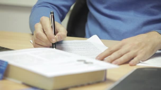 Empresário em sua mesa lendo um documento de texto com cuidado e faz anotações caneta esferográfica. Antes dele é um livro . — Vídeo de Stock