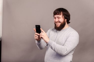 Mutlu genç adam gri arka plan önünde ayakta selfie alarak sakallı