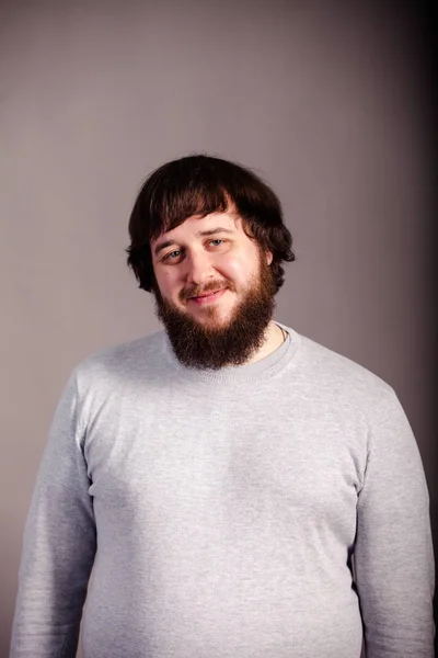 Confiante, homem de sorte com barba na frente de fundo cinza — Fotografia de Stock