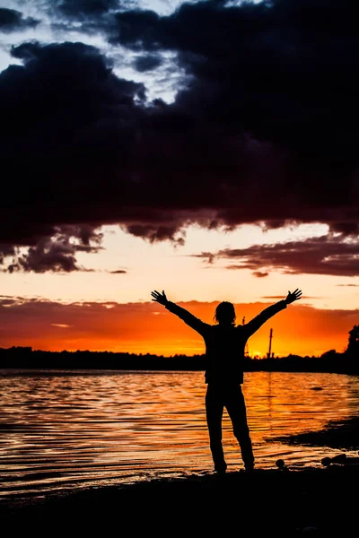 Silhouette di un uomo in piedi su un tronco d'albero nella pausa riva di una spiaggia con le mani alzate mentre il sole sorge sullo sfondo . — Foto Stock