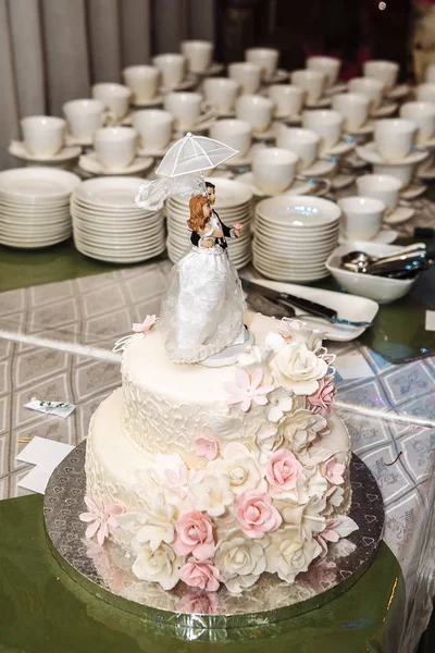 Un pastel de boda blanco multinivel con flores y figuritas de color rosa —  Fotos de Stock