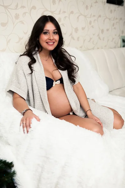 Belle femme enceinte gardant ses mains sur le ventre tout en étant assis sur le canapé . — Photo