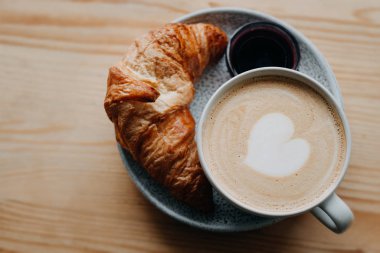 Bir bardak kapuçino ve ahşap pencere kenarında kruvasan.