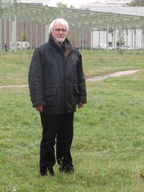 Dışarıda parkta duran uzun siyah deri ceketli beyaz sakallı son sınıf öğrencisinin tam boy portresi.