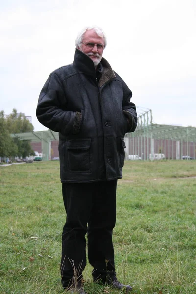 白い髭のシニアの肖像画を閉じ 眼鏡と長い黒い革のコートが公園の外に立っています — ストック写真