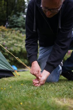 Çimlere çadır kuran erkek ellerini kapatın. Kazıkla çadır kurmak.