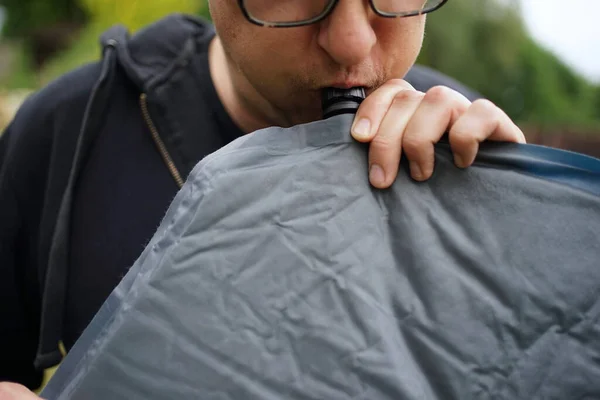 Close up of man with glasses blowing up a self inflatable sleeping pad for camping