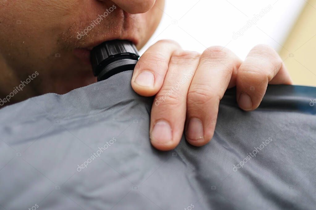 Close up of man blowing up a self inflatable sleeping pad for camping  