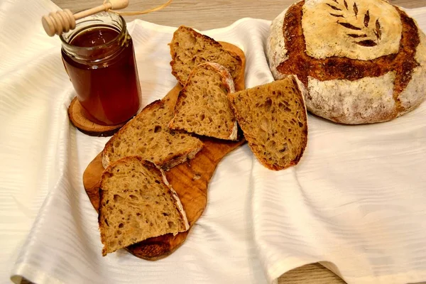 Sliced homebaked sourdough bread with honey jar on table cloth