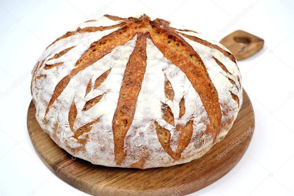 Home baked rye sourdough bread, decorated with hand scoring on wooden board and white background