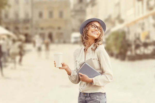 Городская литература. Счастливая молодая студентка с кофе на вынос, с книгами для чтения и учебы на фоне города . — стоковое фото