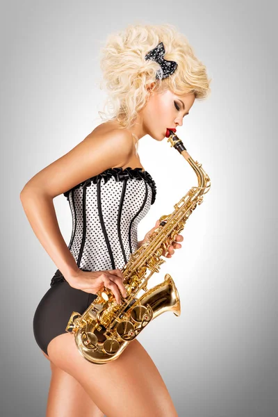 Spiller jazz. Vakker pinup-modell som spiller saksofon på grå bakgrunn . – stockfoto
