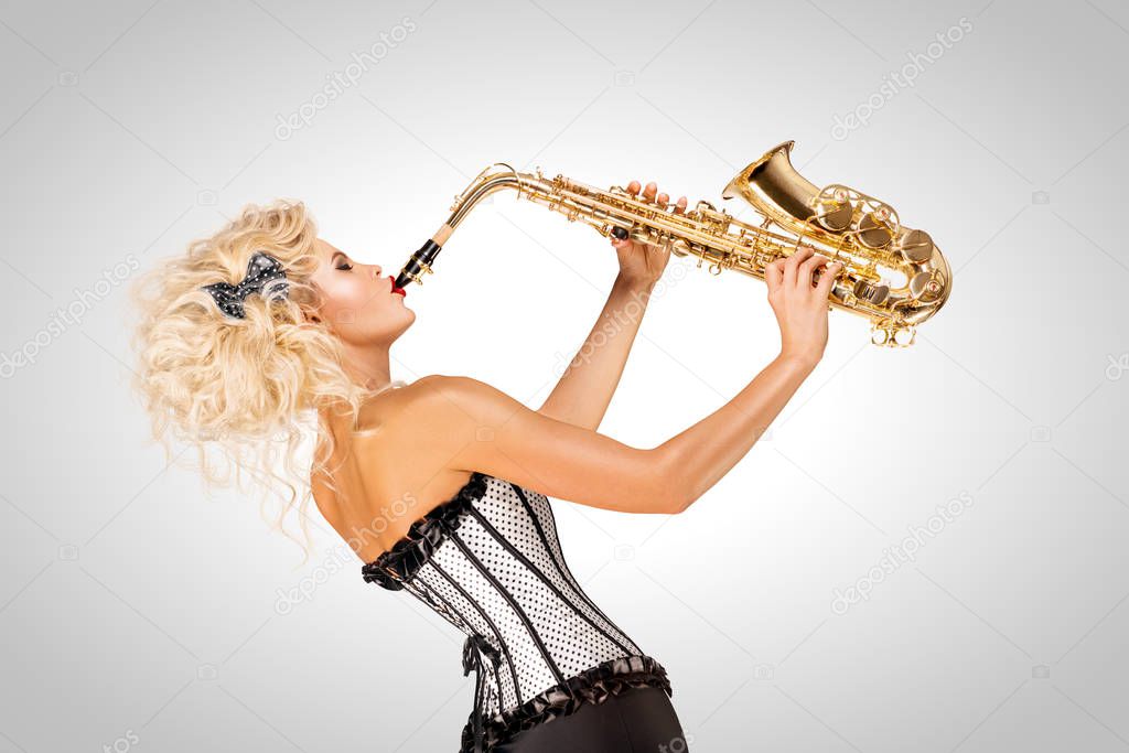 Playing jazz. Beautiful pinup model playing saxophone on grey background.