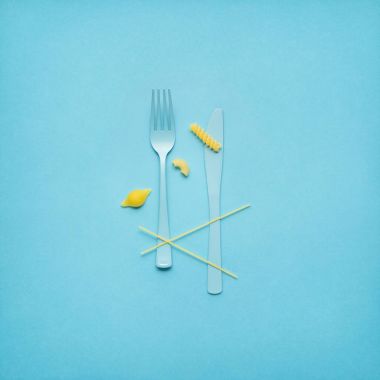 Lezzetli makarna. Çatal ve kaşık pişmemiş makarna üzerine mavi arka plan ile yaratıcı natürmort fotoğrafı.