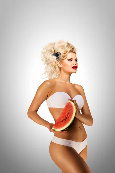 Bikini och vattenmelon. Vackra pinup bikini modell, hålla en vattenmelon på grå bakgrund. — Stockfoto