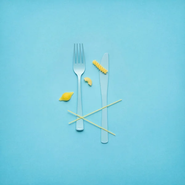 Tasty pasta. Creative still life photo of fork and spoon with raw pasta on blue background. — Stock Photo, Image