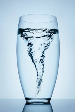Magnificent tornado made of water in a transparent glass standing on the reflective surface.