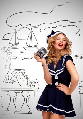 Retro bir göz alıcı pin-up denizci kız poz ve yarım yamalak gri arka plan üzerinde eski bir vintage fotoğraf kamera ile fotoğraf bir deniz kıyısı ve turist çekme fotoğrafı.