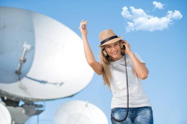 Mutlu genç kadın vintage müzik kulaklık müzik dinlemek ve Kablosuz sinyaller uydulardan alır uydu çanağı çerçevede dans şapkalı.