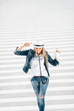 Güzel genç kadın bir paket servisi olan restoran kahve fincanı, zebra geçiş ile yolda duran, kahve içme ve yol arka planı poz ile şapka ve kot pantolon ceket.