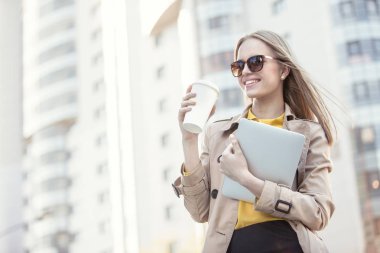 Kahve içme ve tablet Kentsel şehir arka planı onun elinde tutan güzel genç işkadını tek kullanımlık kahve fincanı ile.