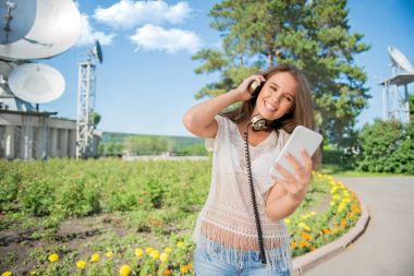Bir smartphone dalga köpüğü enterne ve çerçevede Kablosuz sinyaller uydulardan alan çanak ayakta güzel genç kadın vintage müzik kulaklık boynuna,.