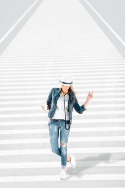 Güzel genç kadın bir paket servisi olan restoran kahve fincanı, zebra geçiş ile yolda duran, kahve içme ve yol arka planı poz ile şapka ve kot pantolon ceket.