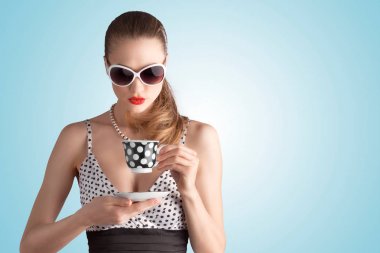 Benekli elbise ve bir bardak tutan güneş gözlüğü pin-up kızı fotoğrafı.
