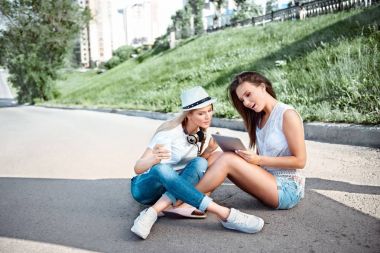 Paket servisi olan restoran kahve ile yolda oturan ve bir telefonu kullanarak, selfie yapım ve tablet yeşil çim ve bir yol arka plan karşı birlikte net sörf iki çekici genç kadın resimleri bir dizi.