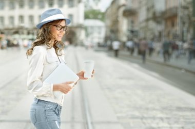 Kahve içme, tablet onun elinde tutan ve Kentsel şehir arka plan karşı karşıya güzel genç kadın ile bir tek kullanımlık kahve fincanı.