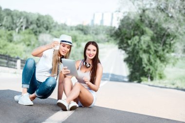 Müzik kulaklık, tablet kullanma ve şehir arka plan karşı çevrimiçi müzik satın alma giyen bir paket servisi olan restoran kahve fincandan kahve içme yolda oturup mutlu genç kadın.