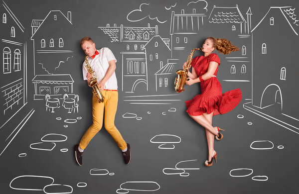 Love story concept of a romantic couple against chalk drawings background. Musician couple playing serenade on saxophone on city streets.