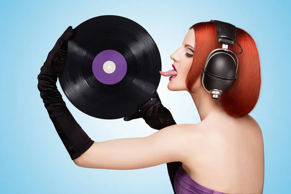 魅惑的な少女 巨大なビンテージ音楽ヘッドフォンを身に着けていると 青の背景に紫 Microgroove ビニール レコードを舐めているのカラフルな写真 — ストック写真