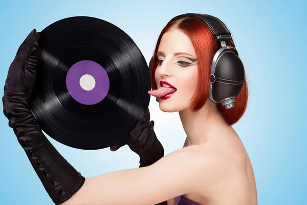 セクシーな女の子 巨大なビンテージ音楽ヘッドフォンを身に着けていると 青の背景に紫 Microgroove ビニール レコードを舐めているのカラフルな写真 — ストック写真