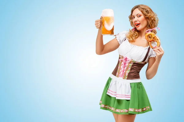 年轻性感的慕尼黑啤酒节女服务员穿着巴伐利亚传统服饰裙提供一个椒盐卷饼和啤酒的杯子 在蓝色背景上 — 图库照片