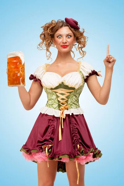 年轻性感的慕尼黑啤酒节女服务员穿着传统的巴伐利亚服饰裙抱着一大杯的啤酒 和有一个想法 在蓝色背景上 — 图库照片