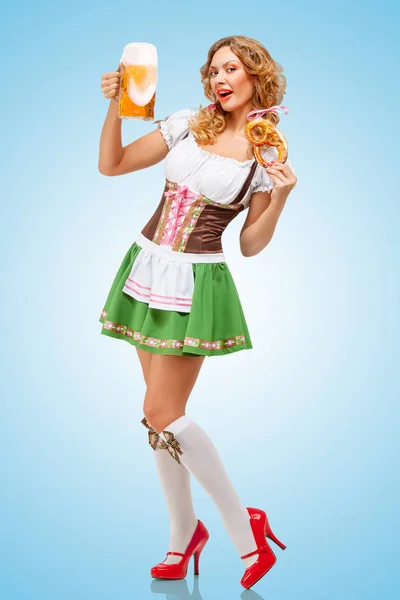 年轻性感的慕尼黑啤酒节女服务员穿着巴伐利亚传统服饰裙提供一个椒盐卷饼和啤酒的杯子 在蓝色背景上 — 图库照片