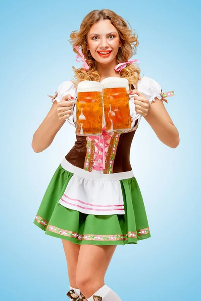 年轻的性感慕尼黑啤酒节的女人 戴着两个啤酒杯全心全意快乐的微笑在蓝色背景的传统巴伐利亚服饰裙 — 图库照片