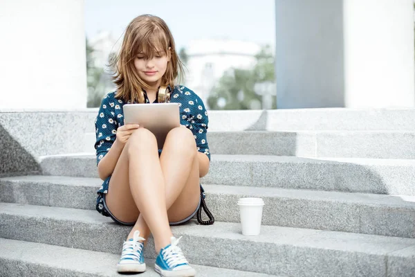 タブレットと階段の上に座ってインターネットをサーフィン音楽ヘッドフォン首周辺テイクアウト コーヒー カップで美しい若い女性 — ストック写真