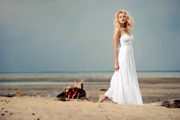 一个赤脚的女人 穿着一件白色的连衣裙明火附近的海滩上 — 图库照片