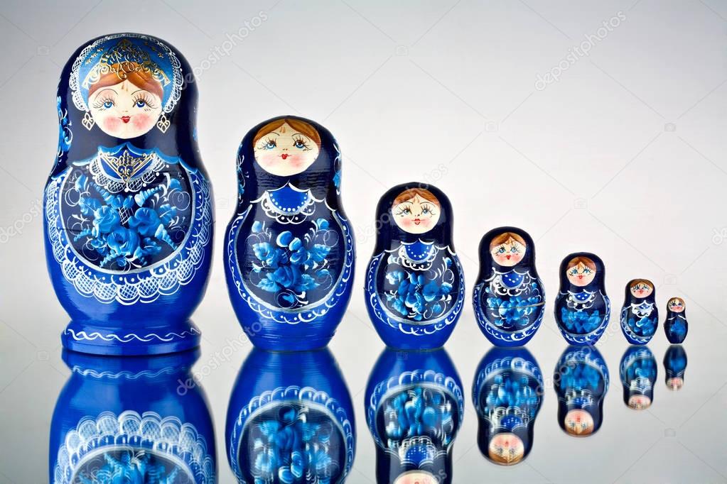 A set of seven blue painted Russian nesting dolls on mirror surface.