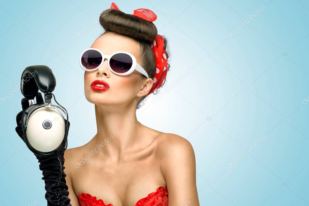 The retro photo of a cute pin-up girl in sunglasses with vintage music headphones.