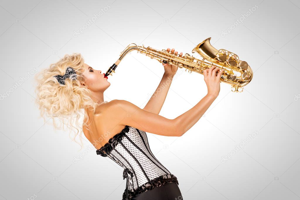 Beautiful pinup model playing saxophone on grey background.